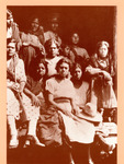 Haunting photo of nine armed women gazing at the viewer. One girl sits on the back of a truck. Most have belts of bullets around their waists. They are dressed in long dresses or skirts.