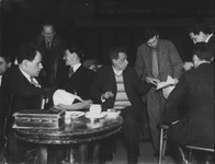 This rare photograph of Eisenstein and Meyerhold together in rehearsal depicts a bustling creative atmosphere with Meyerhold, center, pointing out something on a piece of paper and Eisenstein, left, sitting behind a round table. Those in the photograph—all men—are in jackets and ties, except Meyerhold, who wears a striped sweater under his open blazer.
