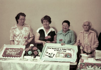 Color photo. Rosies and a quilter stand behind a refreshment table with two sheet cakes and a bouquet of flowers. See Resources for full description.