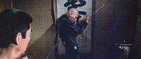A film still of a man being impaled with a sword against a wall-hanging calligraphy scroll.