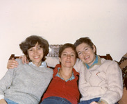 Sitting back on a couch, Korn, Cohen, and Poore smile toward the viewer. Cohen and Poore have short, cropped hair. Korn and Poore wear sweaters. Cohen wears a red corduroy shirt.
