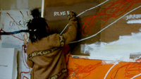 Basquiat writes white text on a wall-mounted painting.