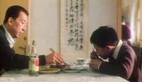 A family dining room is decorated with a scroll with pretty calligraphy. A father and son eat in the foreground.