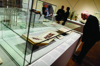 A man on the right examines two open books in a glass-covered case.