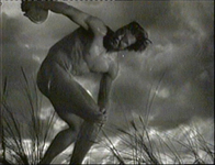 A naked olympian poses in darkness and fog, in black and white cinematography.