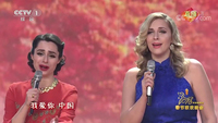 Two young Caucasian women singing the Chinese patriotic song I Love You, China during CCTV’s 2018 Spring Festival Gala. Both look sincerely moved by the song’s sentiments. The blonde woman on the right wears a blue traditional sleeveless cheongsam, and the dark-­haired woman on the right a red dress and gold necklace.