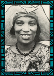Hurston smiles toward the viewer in large, brimmed, floppy cloth hat. She wears a scoop-neck, floral print top accented with a strand of black beads.