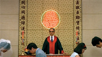 A film still of a neon light calligraphic character on a patterned wall, framed by vertical black calligraphy, behind a man in a tie and black-and-red robes and couples bowing to each other.