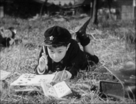 A student lies in a field writing black calligraphy, in black and white cinematography.