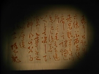 A page of parchment has red calligraphy written on it, with a candle casting a candlelight circle on it.