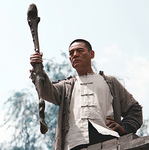 Dai Tianli, the anti-­Japanese hero of The Dog-­beating Staff, standing atop a wall with one hand on his hip and the other holding aloft an approximately 40-­inch-­long stick known as the dog-­beating staff. He looks determined.