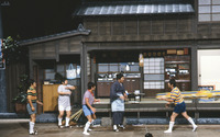 Color photograph of large stage with performers (The Drifters) in front of Japanese style home. Ikariya Chōsuke is dressed as the mother, while other members are dressed as children.