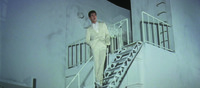 A low-­angle long shot of Tetsu on the steps of the building. The frame is dominated by whiteness, from Tetsu’s suit to the façade and contours of the building, that dominates the entire background but for a tiny corner of night sky. Tetsu has an easy, breezy stance as he sings the title tune (in voiceover).