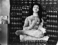 The staged photograph represents the doll seated in a lotus position, looking up, meditating (and perhaps even levitating), next to a sketch of a head, presumably by Kokoschka.