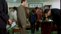 A group bows in an office in front of a banner on the wall with black calligraphy printed on it.