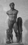Larger-than-life-size black basalt statue of a standing Hercules. He is nude and has his head turned to its right. Arms missing. Tree trunks at both flanks, the right one covered by his lion skin and supporting his club