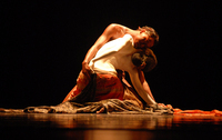 Figure 10.1. In warm light, a man and woman sit on stage facing each other, torsos naked and sensuously pressed together, melting to one side, fabric covering their hips and legs.