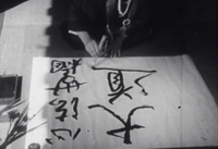 A man paints black calligraphy on white paper, in black and white cinematography.