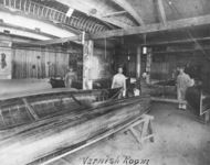A black-and-white photograph of workers in the Canadian Canoe Company factory applying varnish to canoes.