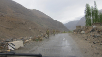 Six Tajik border guards marching along the side of an asphalt road near Shughnan district, Tajikistan’s border crossing. They have green camouflage uniforms and are holding AK-47 machine guns.