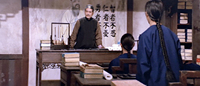 Two students in the foreground and midground are scolded by their instructor in the background in a Confucius school. Black calligraphy is written on the wall behind the instructor (the three virtues from the Analects of Confucius—9th Chapter Zihan), next to a drawing of Confucius.