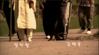 A procession of feet walking down a path has white titles calligraphy superimposed over it.