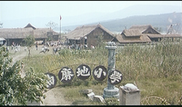 People run among buildings with thatched roofs, surrounded by fields. An archway with calligraphy is visible at the bottom foreground.