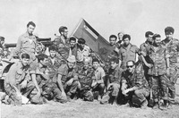 Black and white photo of light and dark-­skinned IDF soldiers posing together with a captured Jordanian flag and other loot from battle.