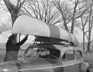A photograph of a canoe strapped to the top of a car.