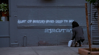 A character writes graffito on a grey wall: "A lot of Bowery bums used to be executives."