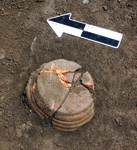 Photograph of an upside down brown pot placed on the dirt and below a black and white printed arrow pointing to the upper left.