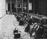 Photograph depicting a row of lighting and projection units backstage, with offstage wing visible at the top of the photograph.