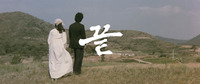 A film still of white calligraphic text over the background of two people standing on a hill overlooking a hilly, rural landscape.