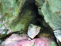 Entryway of Shpella e Hudhrës, a large rock sits in front of the rocky cave entrance.
