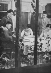 A black-­and-­white photograph of Taiwon Koh, her husband, and her three kids, sitting at a table. Koh and her husband look on while their kids engage in their studies