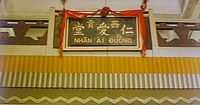 A close-up of a placard with the name of a store in gold calligraphy, with a red ribbon framing it. One of the main characters wants to take his store name with him back to Hong Kong.