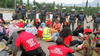 A group of people, many of them wearing #BringBackOurGirlsNow merchandise, sit in the middle of a road. A row of police officers stands in front of them, many of them locking arms with one another.