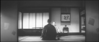 A large work of calligraphy decorates a tokonoma before two samurai. This modernist Japanese director plays with symmetry, placing his characters in the middle and framed by two fusama sliding doors; however, the scroll painting is prominently sitting on the right side of the frame.