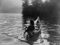 A black-and-white of a figure paddling a dugout canoe.