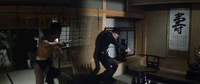 Two men fight with sword and knife inside a room. In the background, calligraphy can be seen on the wall.
