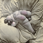 The hand-tinted black and white photograph from The Games of the Doll series (1938-1949) by Hans Bellmer shows a truncated doll body made of two duplicate pelvises, assembled around an abdominal sphere, and arched over a duvet or pillow.