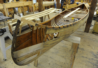 A color photograph of a wood and canvas canoe in the process of restoration.