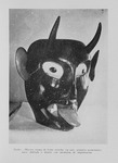 Photograph of a painted wooden mask with two horns coming out of the head, and large eyes. The mouth is partially open with the tongue protruding.