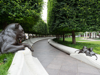 Photograph of the National Law Enforcement Officers Memorial, featuring a statue of a lion overlooking two lion cubs playing, a long curved wall, a paved path, and a long curved bench facing the wall. Along each side of the memorial is a row of trees, and above the long curved wall is a series of wreaths.