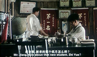Two people in an office, with many plaques and banners with calligraphy in the background. White calligraphy and roman subtitles are at the bottom.