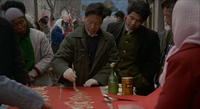 People watch as a man in gloves and coat paints calligraphy onto a red banner.