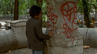 White chalk is written on a public monument covered in red graffiti.