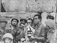 IDF chief Rabbi blows the shofar at the Western Wall flanked by light and dark-­skinned IDF soldiers wearing various uniforms and tefillin.