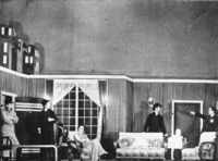 Photograph depicting five actors on the set of an apartment interior, with backdrop visible above wall flats.