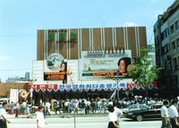 A large billboard for a Korean Film with many people on the busy street looking up towards it.